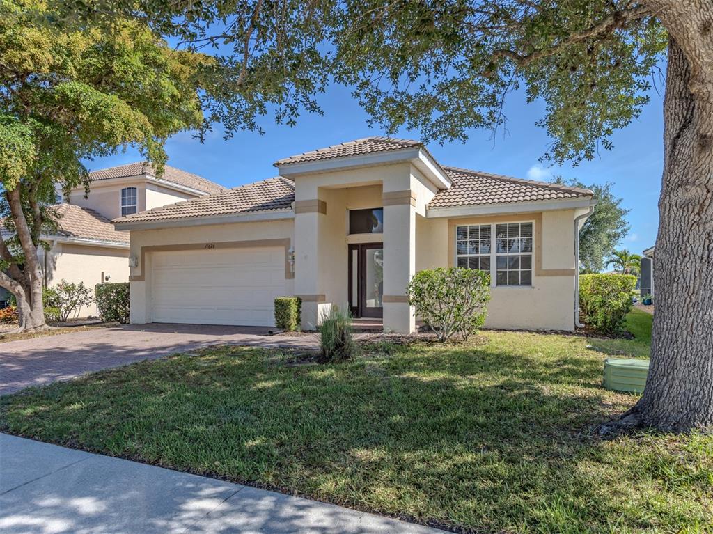 A single-story house with a beige stucco exterior, a tile roof, and a two-car garage — 11626 DANCING RIVER DRIVE, VENICE, FL