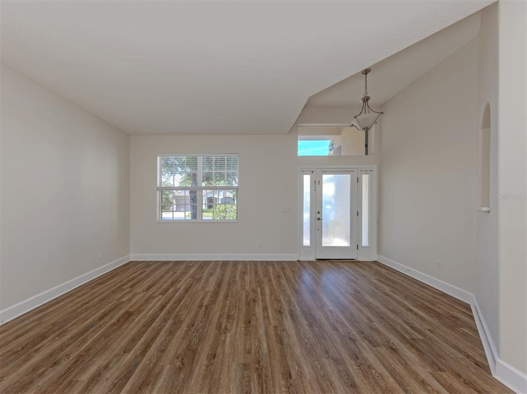 An empty room with wood-look flooring, a window, and a front door with a transom — 11626 DANCING RIVER DRIVE, VENICE, FL