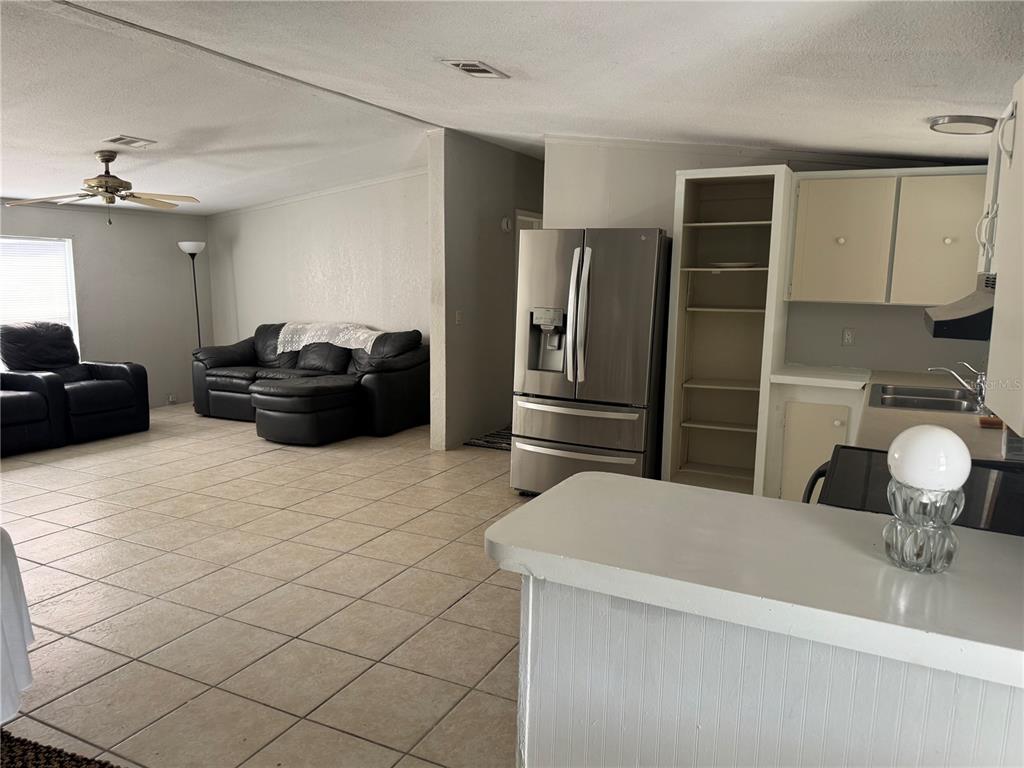 A living room with tile floors and a black sofa opens into a kitchen area — 5406 SYDNEY STREET, PORT ORANGE, FL