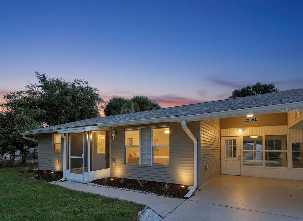 A single-story house with tan siding, a screened-in porch, and an attached carport at dusk — 22392 BUFFALO AVENUE, PORT CHARLOTTE, FL
