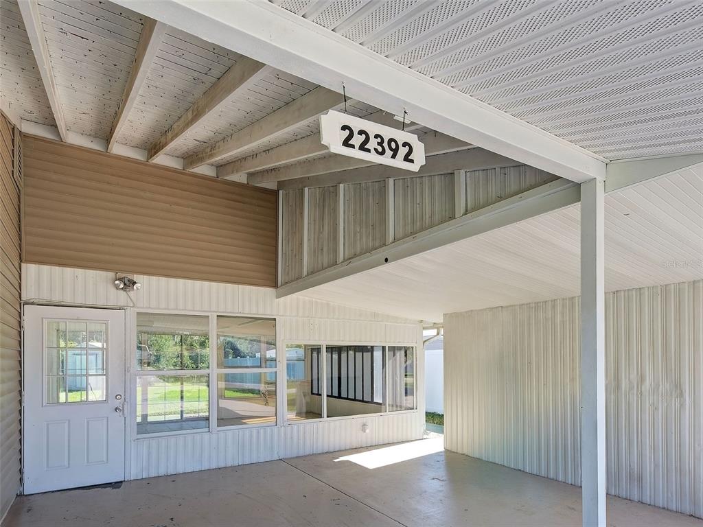 A covered carport area features a white door, large windows, and a hanging address sign — 22392 BUFFALO AVENUE, PORT CHARLOTTE, FL