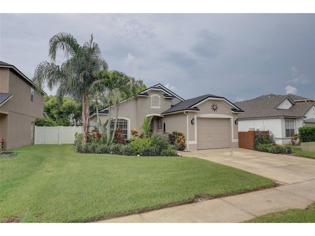 A single-story suburban house with a tan stucco exterior, a two-car garage, and palm trees — 8252 CRESCENT MOON DRIVE, NEW PORT RICHEY, FL