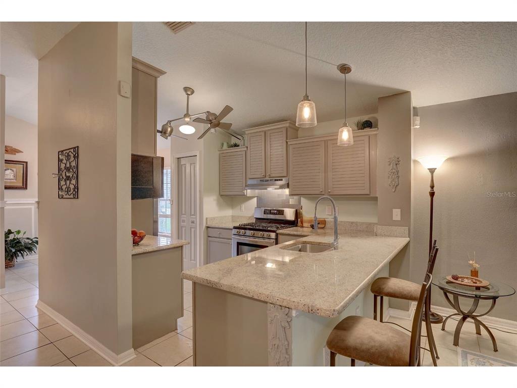 A kitchen with light-colored cabinets, granite countertops, a breakfast bar, and two pendant lights — 8252 CRESCENT MOON DRIVE, NEW PORT RICHEY, FL