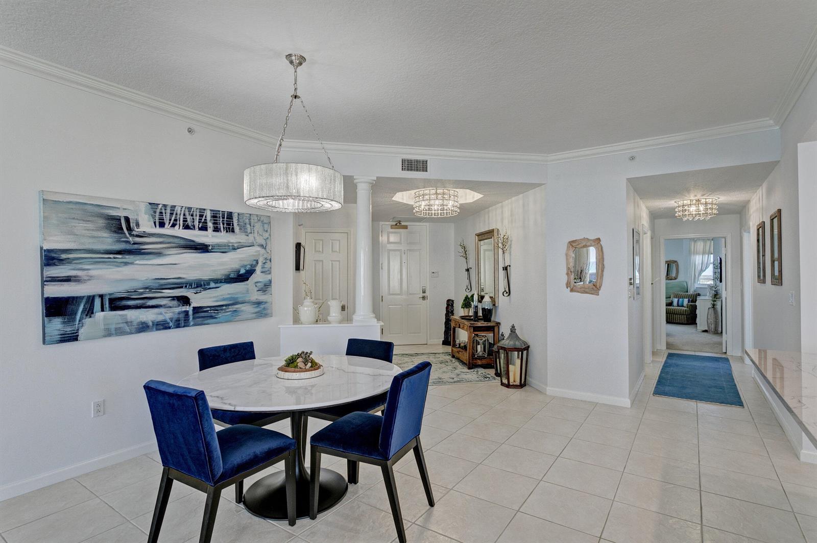 A dining area with a round marble table and blue chairs sits near an entryway — 221 Ocean Grande Boulevard # 701, Jupiter FL 33477, JUPITER, FL