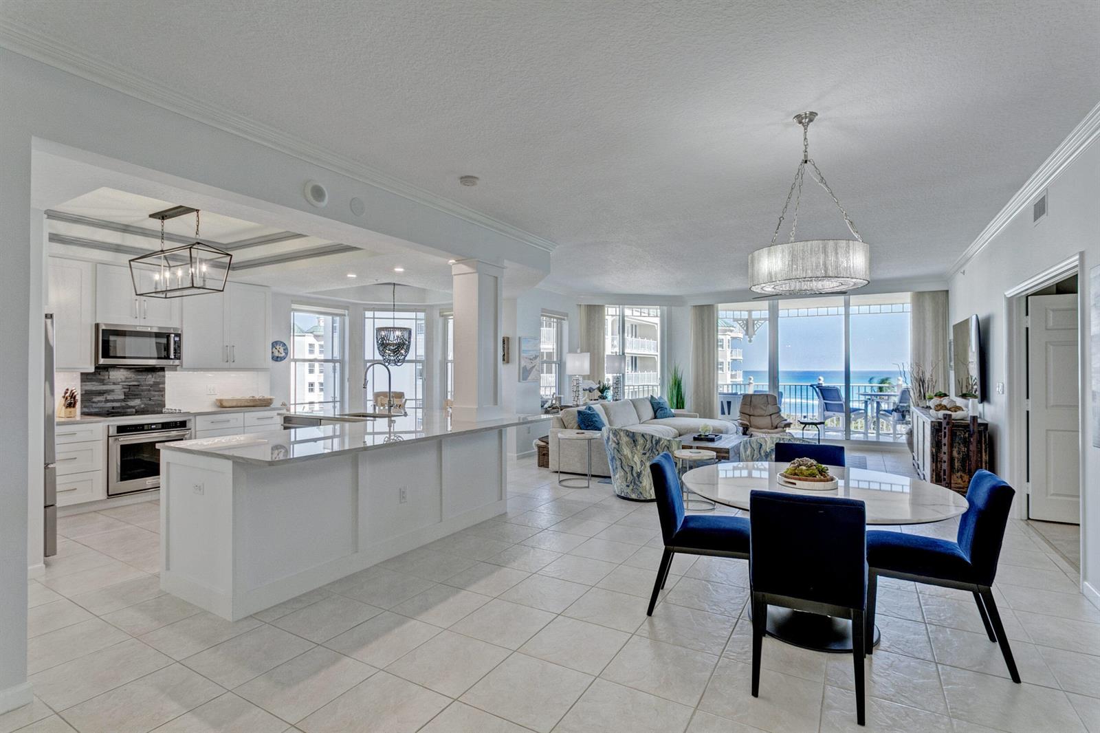 An open-concept kitchen, dining area, and living room feature white cabinetry, tile floors, and ocean views — 221 Ocean Grande Boulevard # 701, Jupiter FL 33477, JUPITER, FL