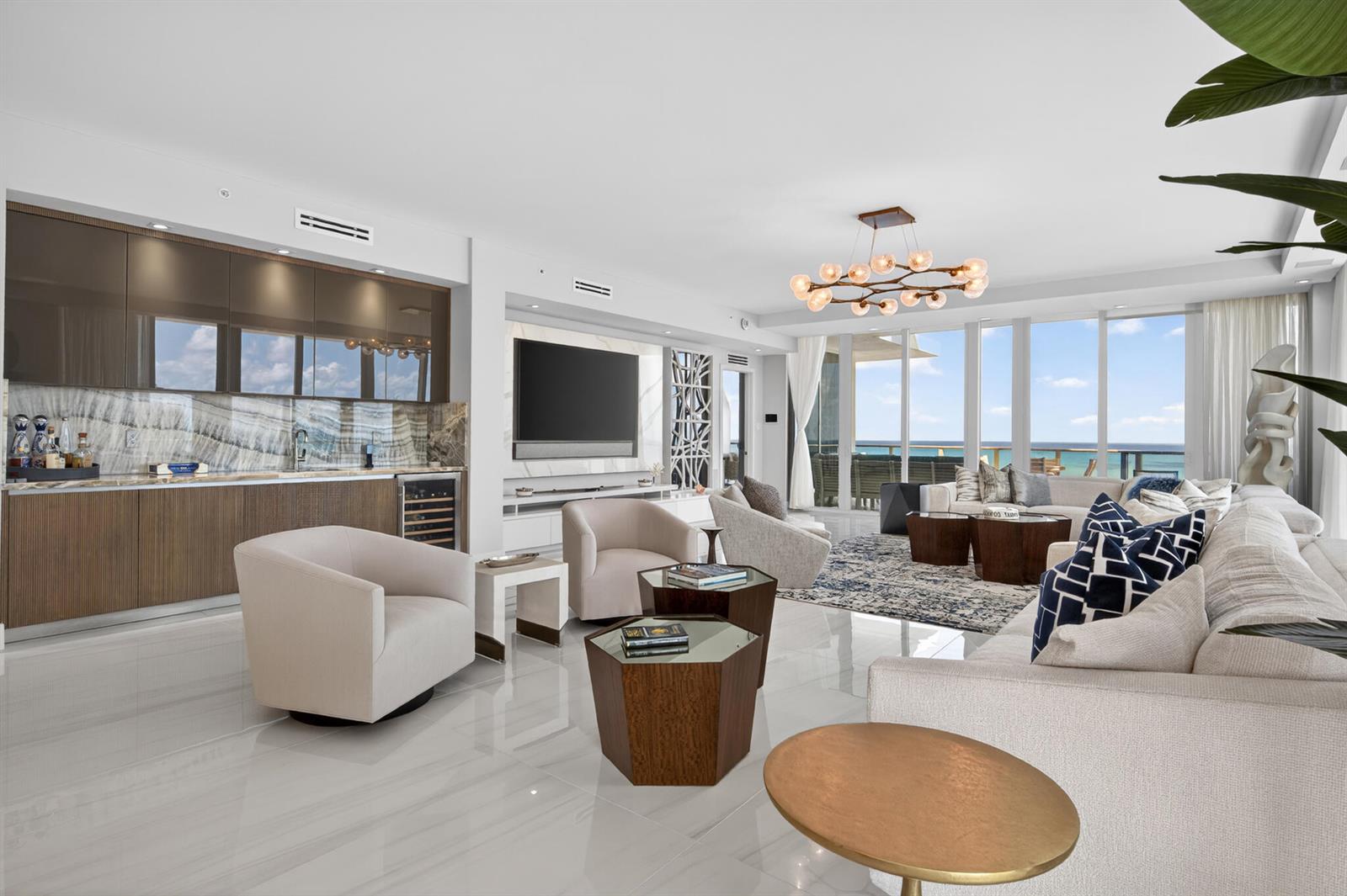 A modern living room features a wet bar, neutral seating, and floor-to-ceiling ocean view windows — 3100 N Ocean Drive, Riviera Beach FL 33404, RIVIERA BEACH, FL