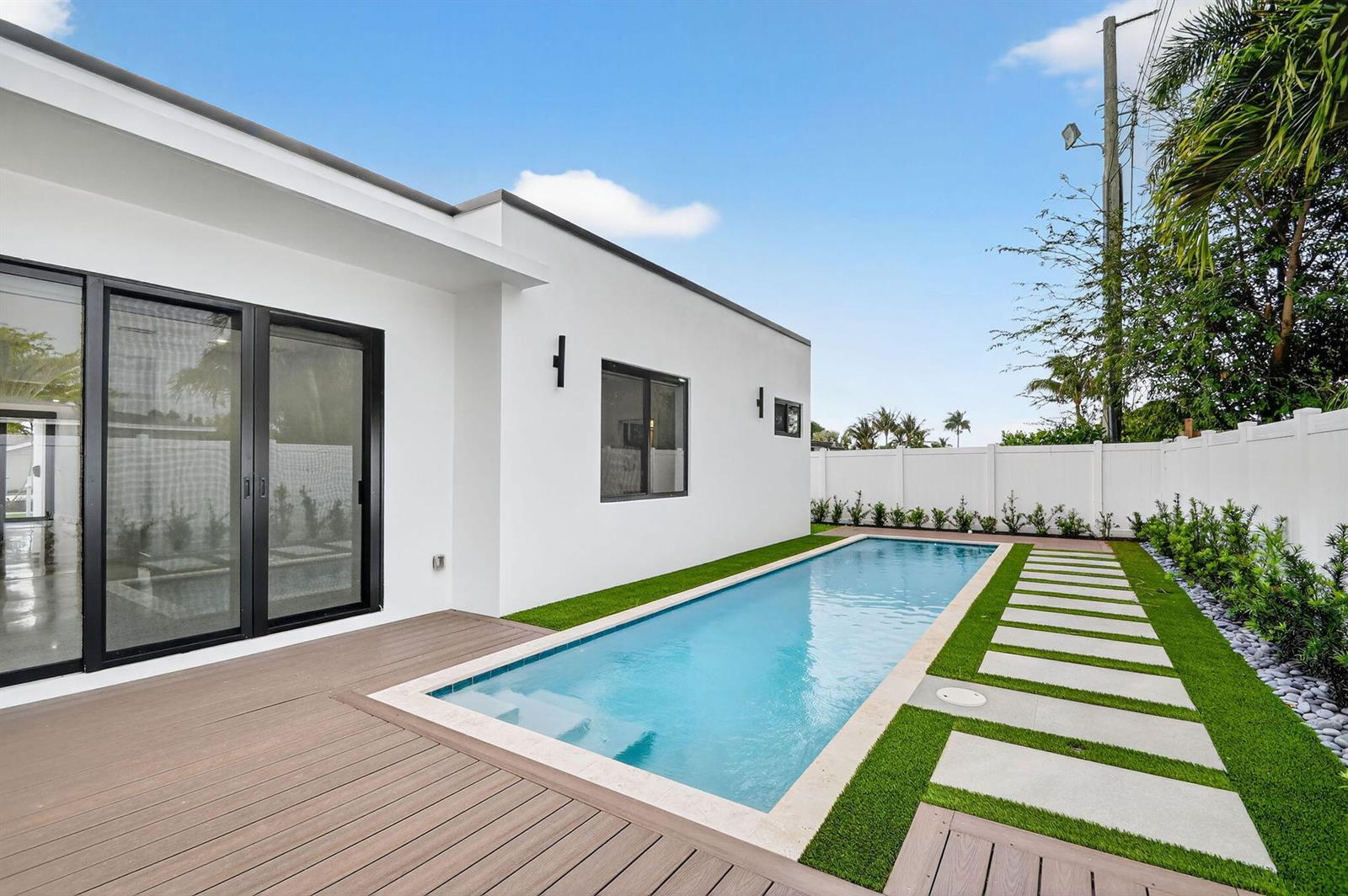 A modern white house exterior features a rectangular swimming pool, wood decking, and stone pavers — 504 Flotilla Road, North Palm Beach FL 33408, NORTH PALM BEACH, FL