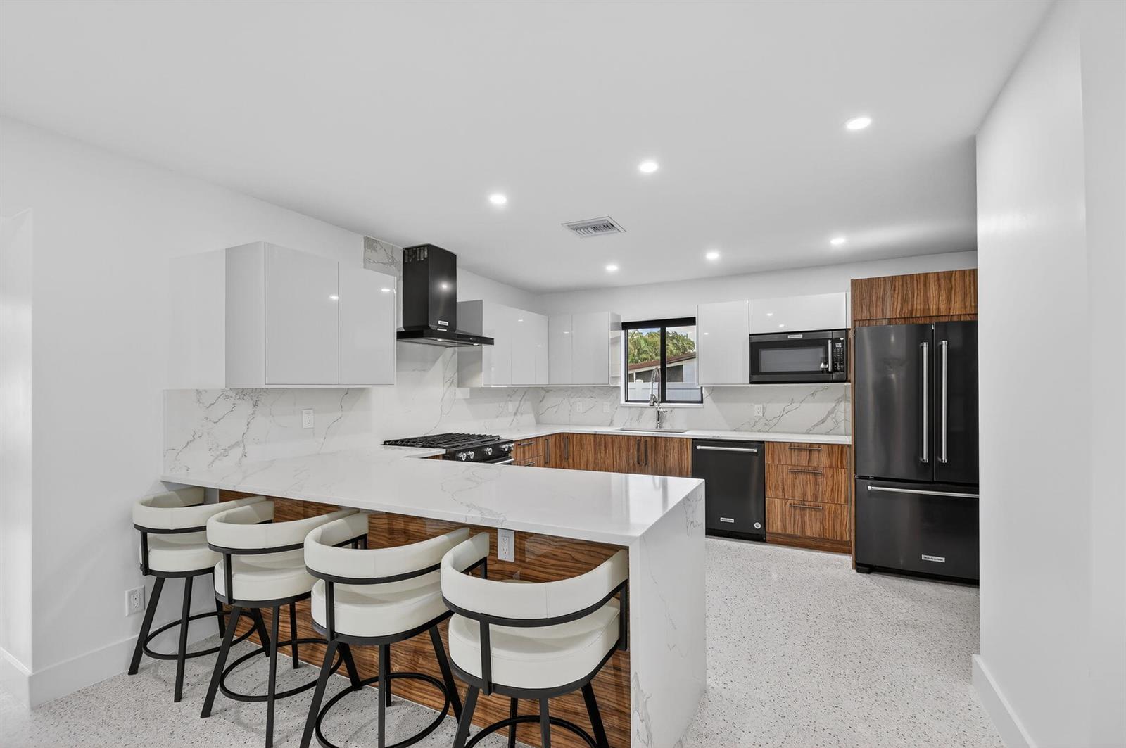 A modern kitchen features white and wood-grain cabinets, a marble-patterned island, and black appliances — 504 Flotilla Road, North Palm Beach FL 33408, NORTH PALM BEACH, FL