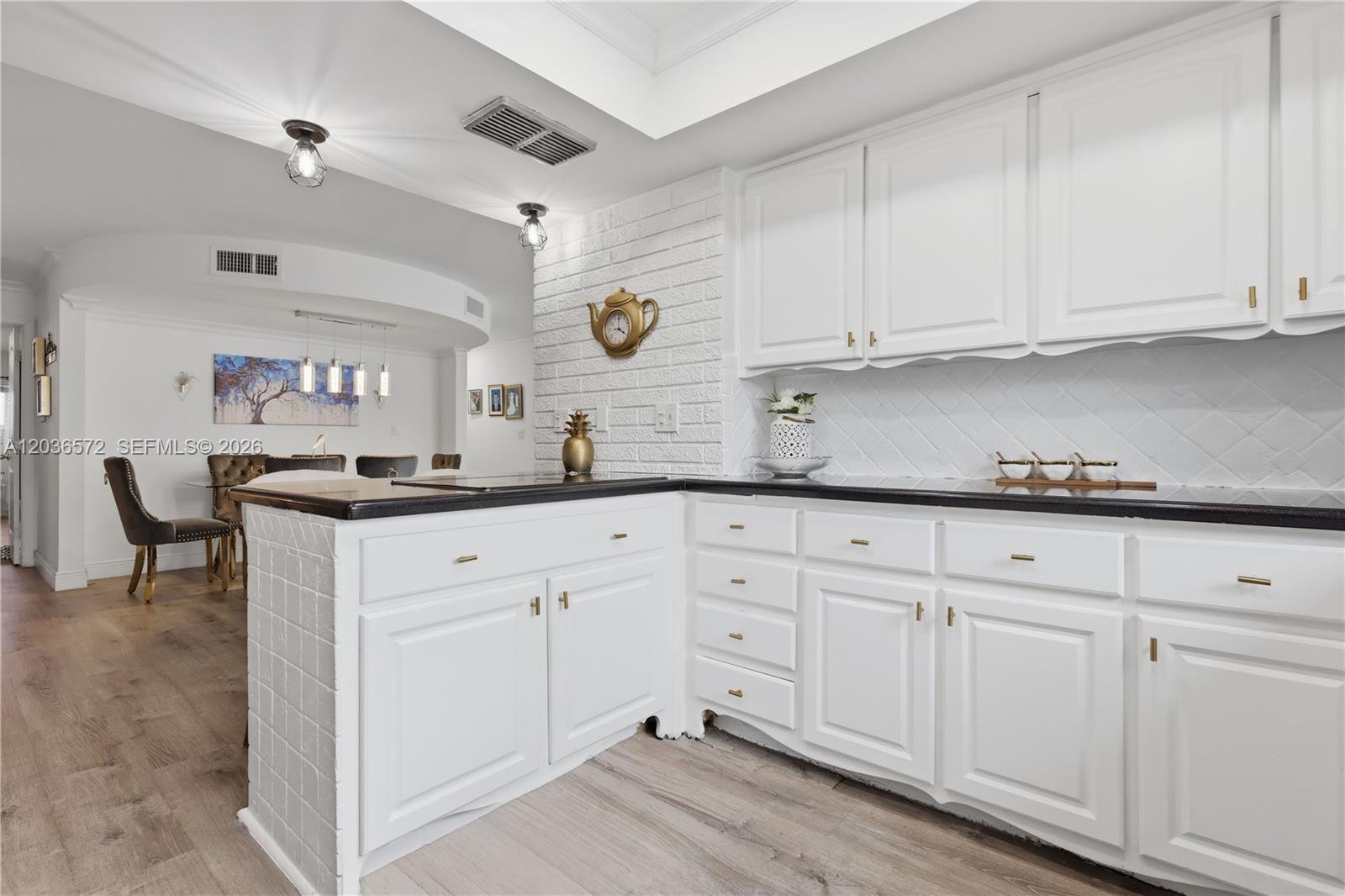 A kitchen features white cabinets, black countertops, and a white brick accent wall — 1040 Crystal Lake Dr # 3, Deerfield Beach FL 33064, DEERFIELD BEACH, FL