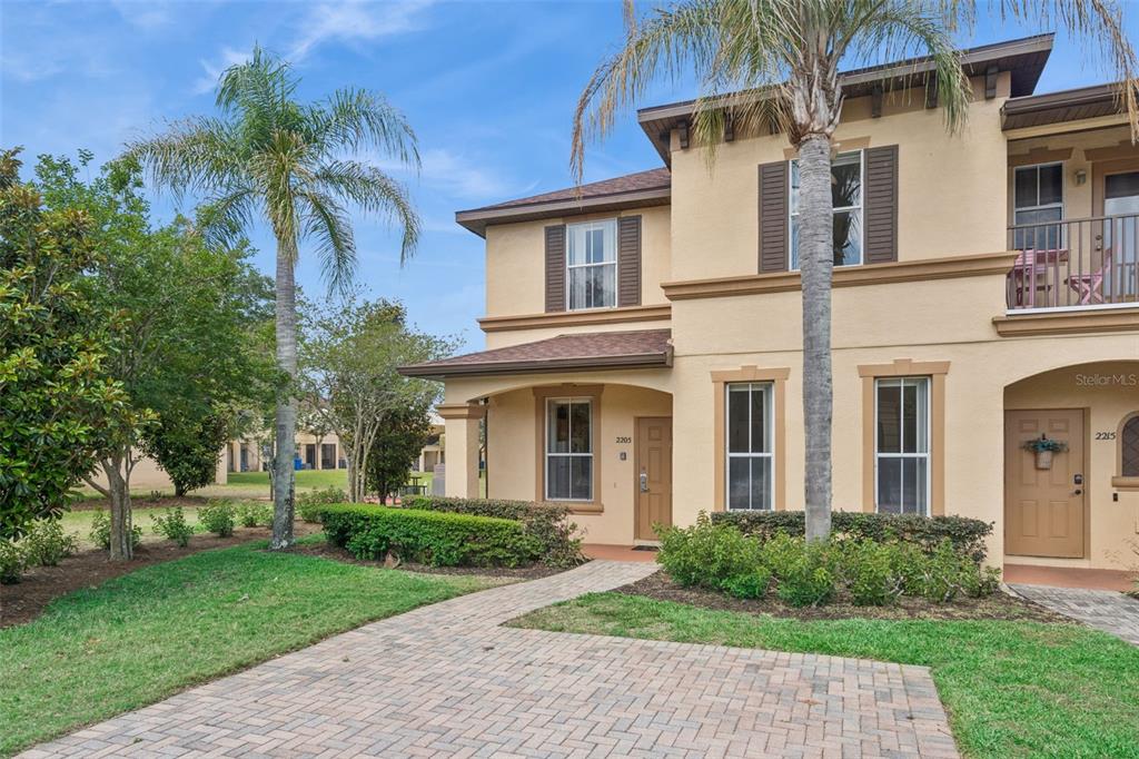 A two-story tan stucco townhouse features a brick paver walkway and palm trees — 2205 CALABRIA AVENUE, DAVENPORT, FL