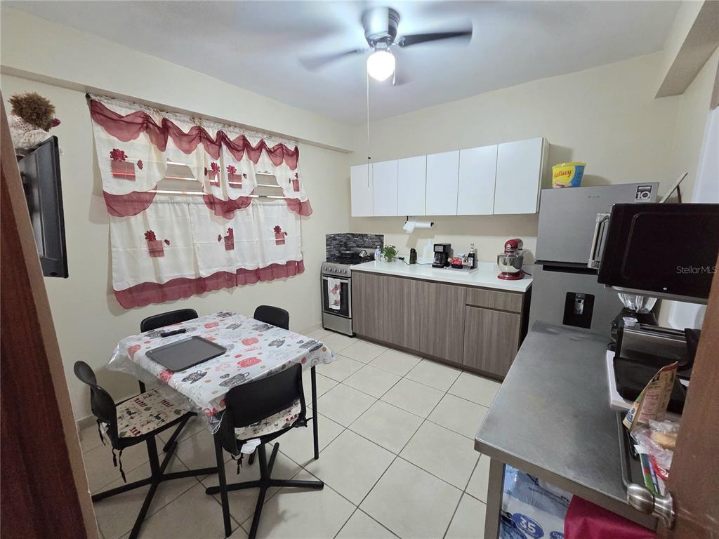 A kitchen with white upper cabinets, wood-look lower cabinets, a dining table, and tile flooring — 173 KM 15.8, CIDRA, PR