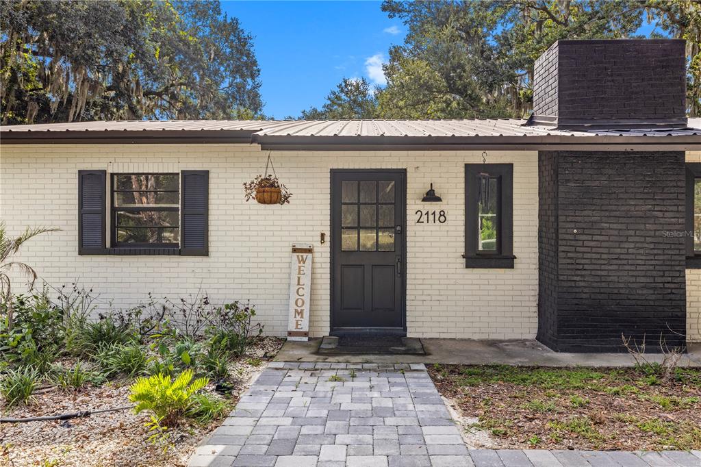 A single-story house exterior features white painted brick, a dark door, and a black chimney — 2118 E KEYSVILLE ROAD, LITHIA, FL