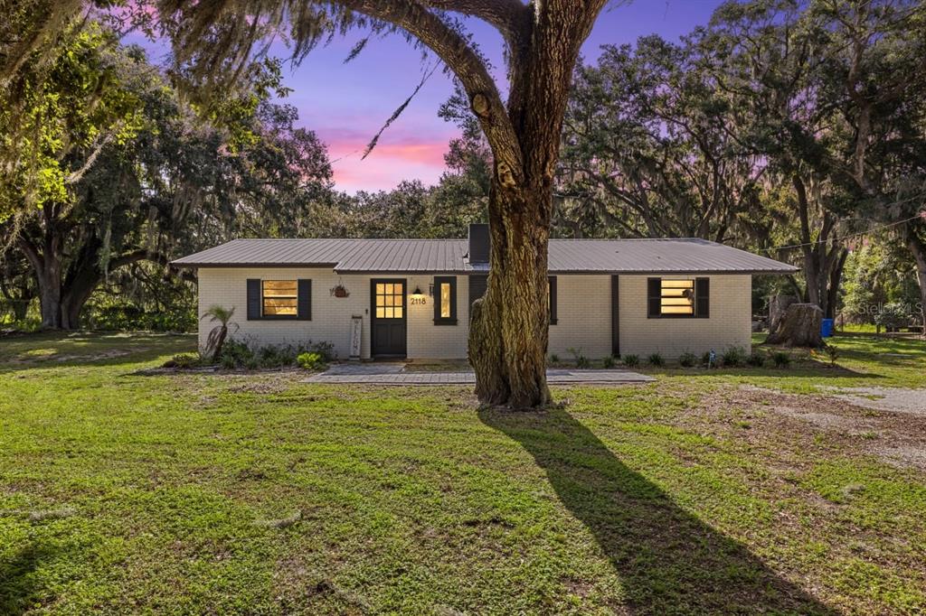 A single-story brick house with a metal roof sits behind a large tree — 2118 E KEYSVILLE ROAD, LITHIA, FL