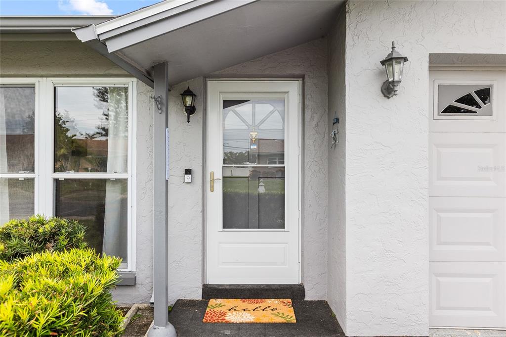 A white front door with a storm door is centered under a small covered porch — 4563 GREAT LAKES DRIVE S, CLEARWATER, FL