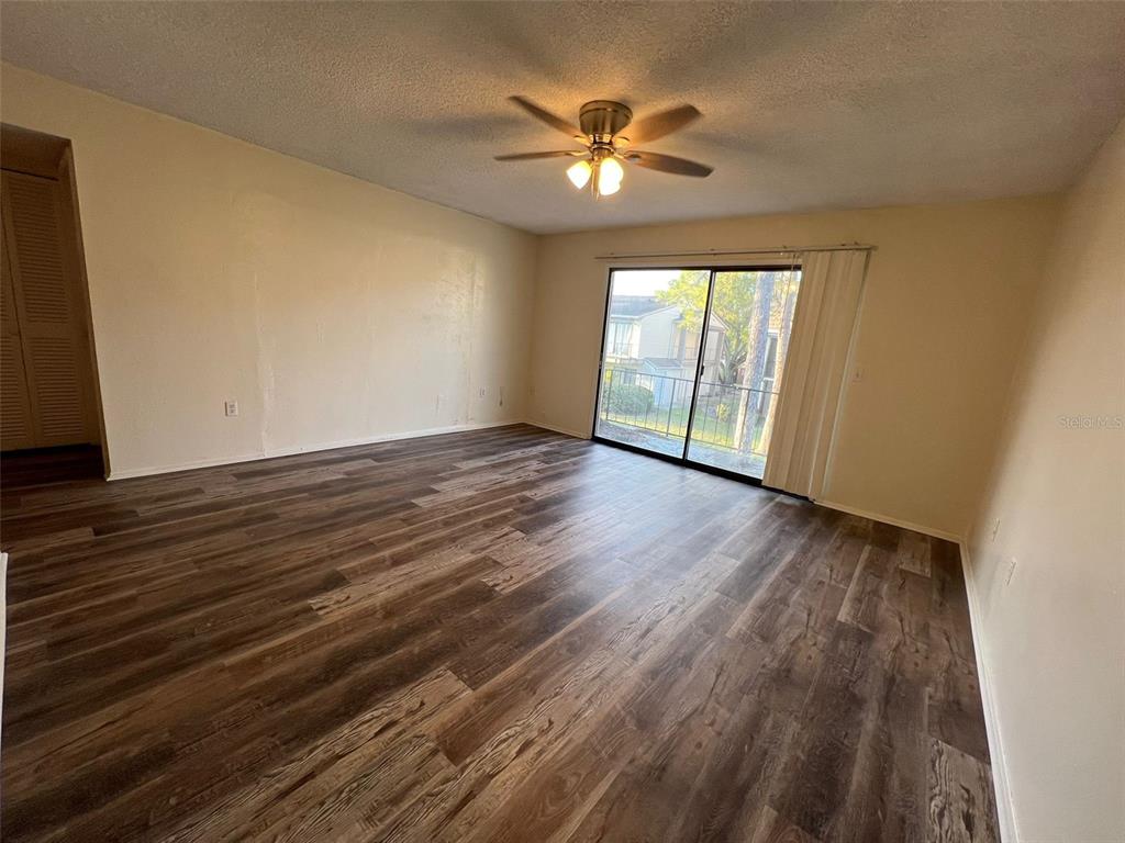 An empty room features wood-look flooring, a ceiling fan, and a sliding glass door — 6043 VILLAGE CIRCLE UNIT 6043, ORLANDO, FL