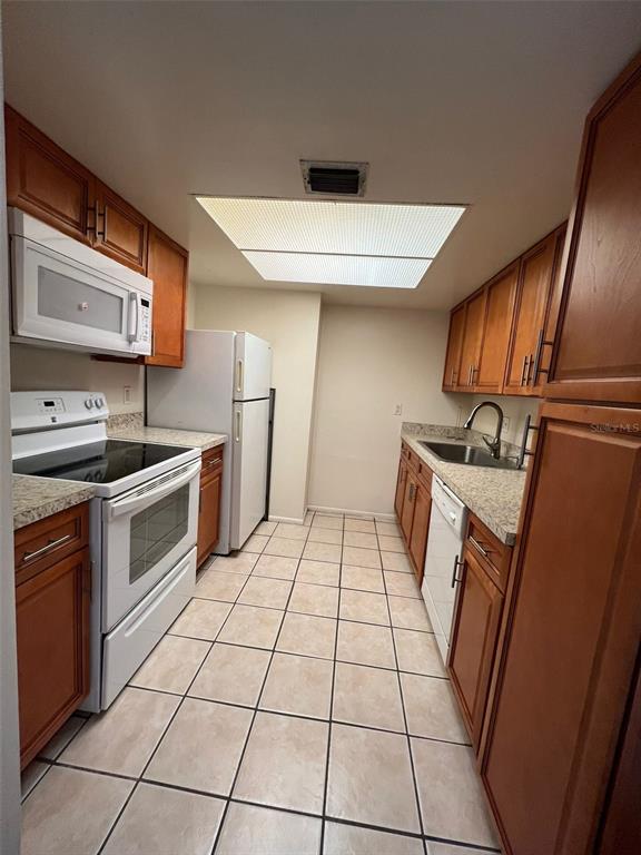 A galley kitchen features wood cabinets, white appliances, granite countertops, and light-colored tile flooring — 6043 VILLAGE CIRCLE UNIT 6043, ORLANDO, FL