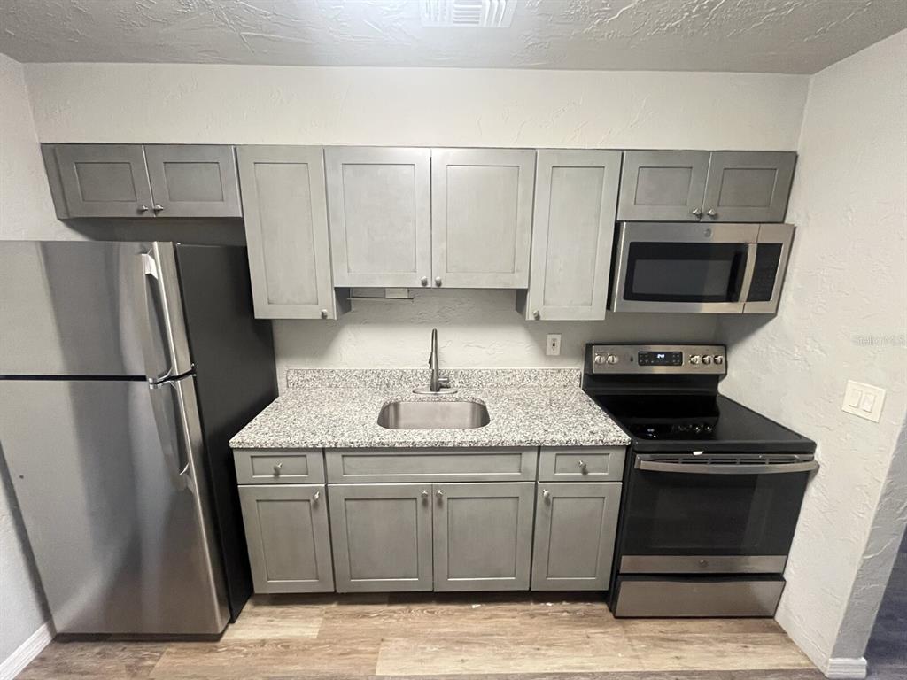 A kitchen features gray cabinets, stainless steel appliances, and a speckled granite countertop — 2519 9TH AVENUE W UNIT 2, BRADENTON, FL