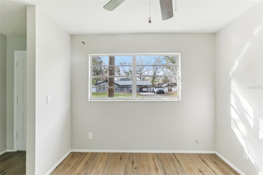 A room with light gray walls, wood-look flooring, and a window overlooking a residential street — 7711 AMHERST STREET UNIT B, TAMPA, FL