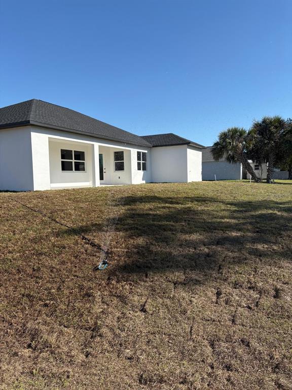 The exterior of a white house with a dark roof and a lawn sprinkler — 1393 RICHMAR STREET, NORTH PORT, FL