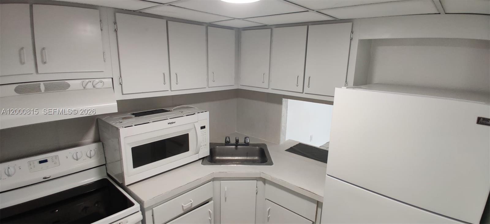 A small kitchen features white cabinets, a white stove, a microwave, and a corner sink — 4550 NW 9th St # 706E, Miami FL 33126, MIAMI, FL