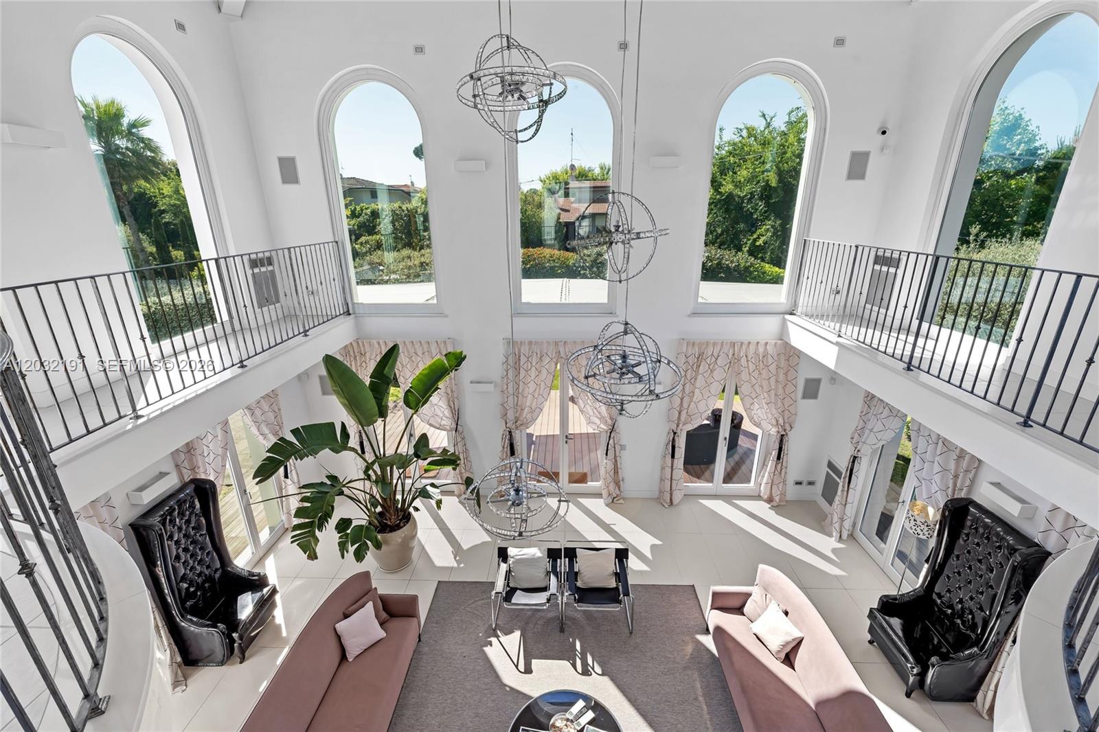 A high-ceilinged living room features arched windows, two black leather chairs, and two sofas — Luxury Real Estate Forte Dei Marmi Max Mlekus, FL