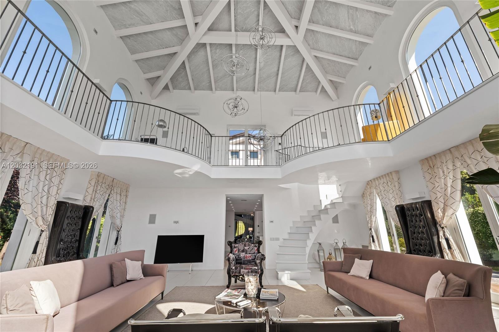 A spacious living room features a vaulted ceiling, a curved mezzanine balcony, and white stairs — Luxury Real Estate Forte Dei Marmi Max Mlekus, FL