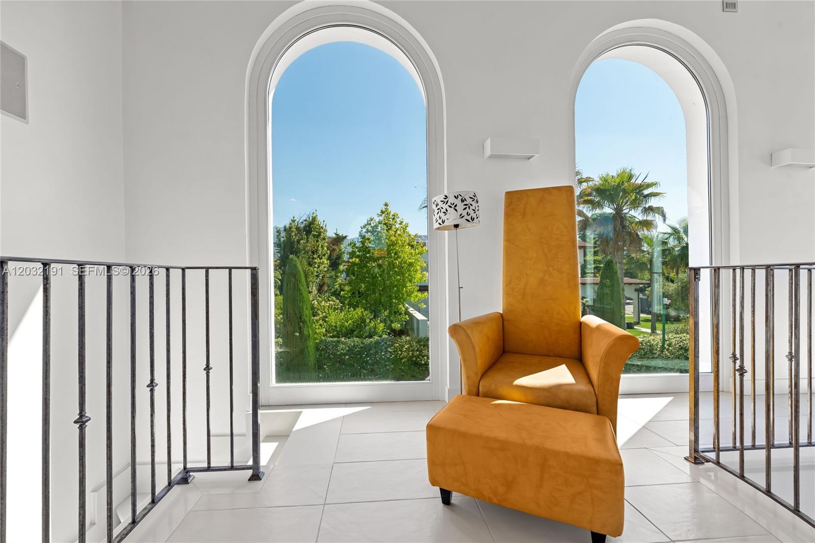 A bright landing features two arched windows, white tile floors, and a tall yellow chair — Luxury Real Estate Forte Dei Marmi Max Mlekus, FL