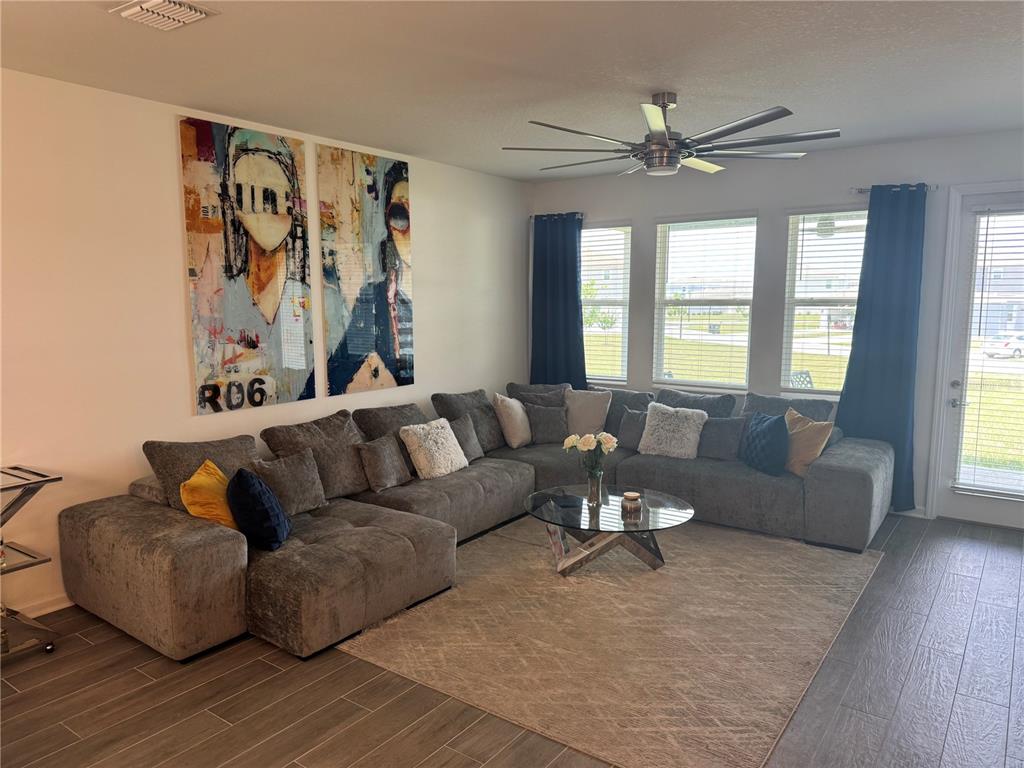 A living room features a large gray sectional sofa, a glass coffee table, and wall art — 2844 ARMSTRONG AVENUE, CLERMONT, FL