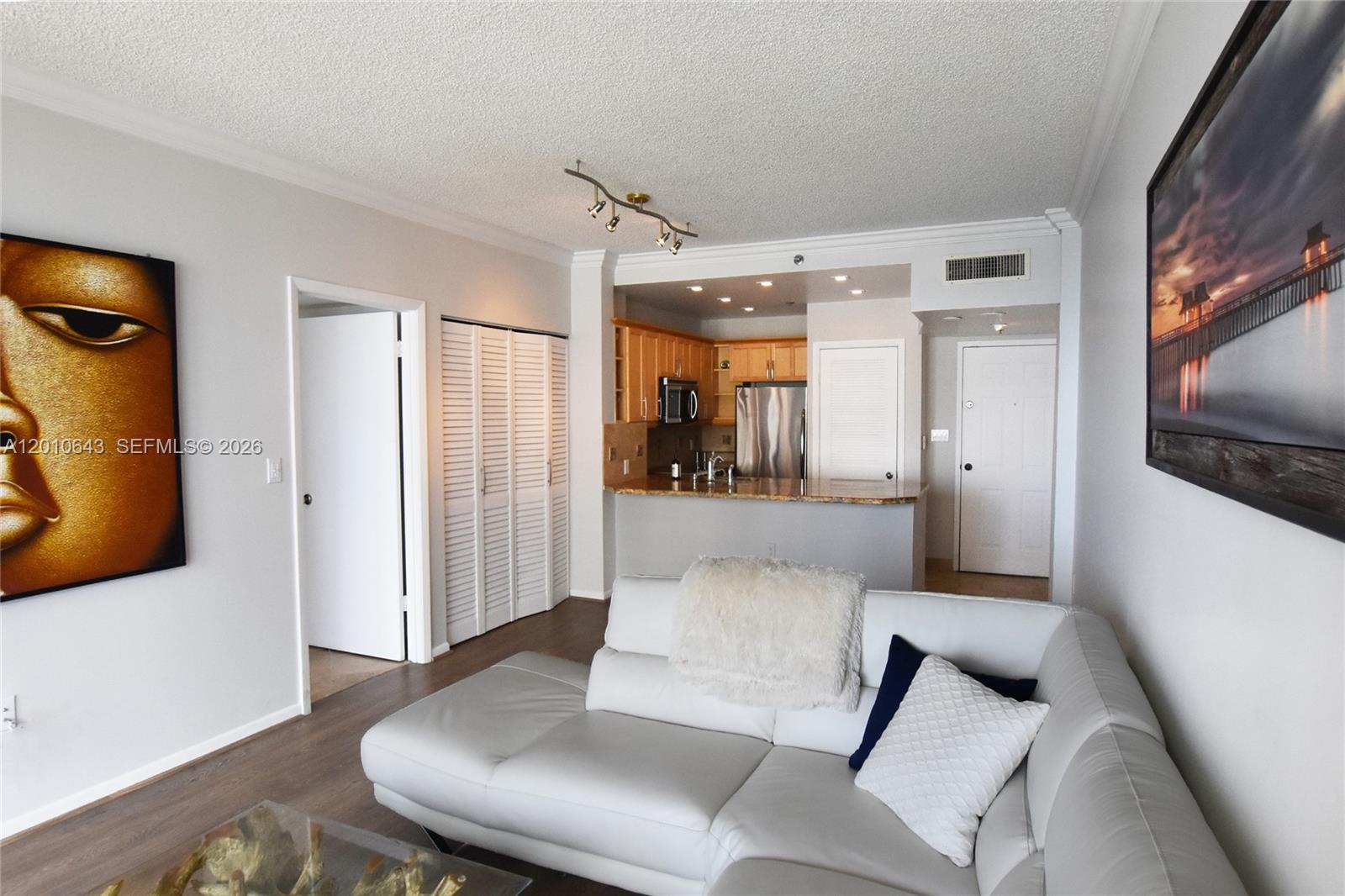 A living room with a white sectional sofa, open kitchen, and two large wall art pieces — 540 Brickell Key Dr, Miami FL 33131, MIAMI, FL