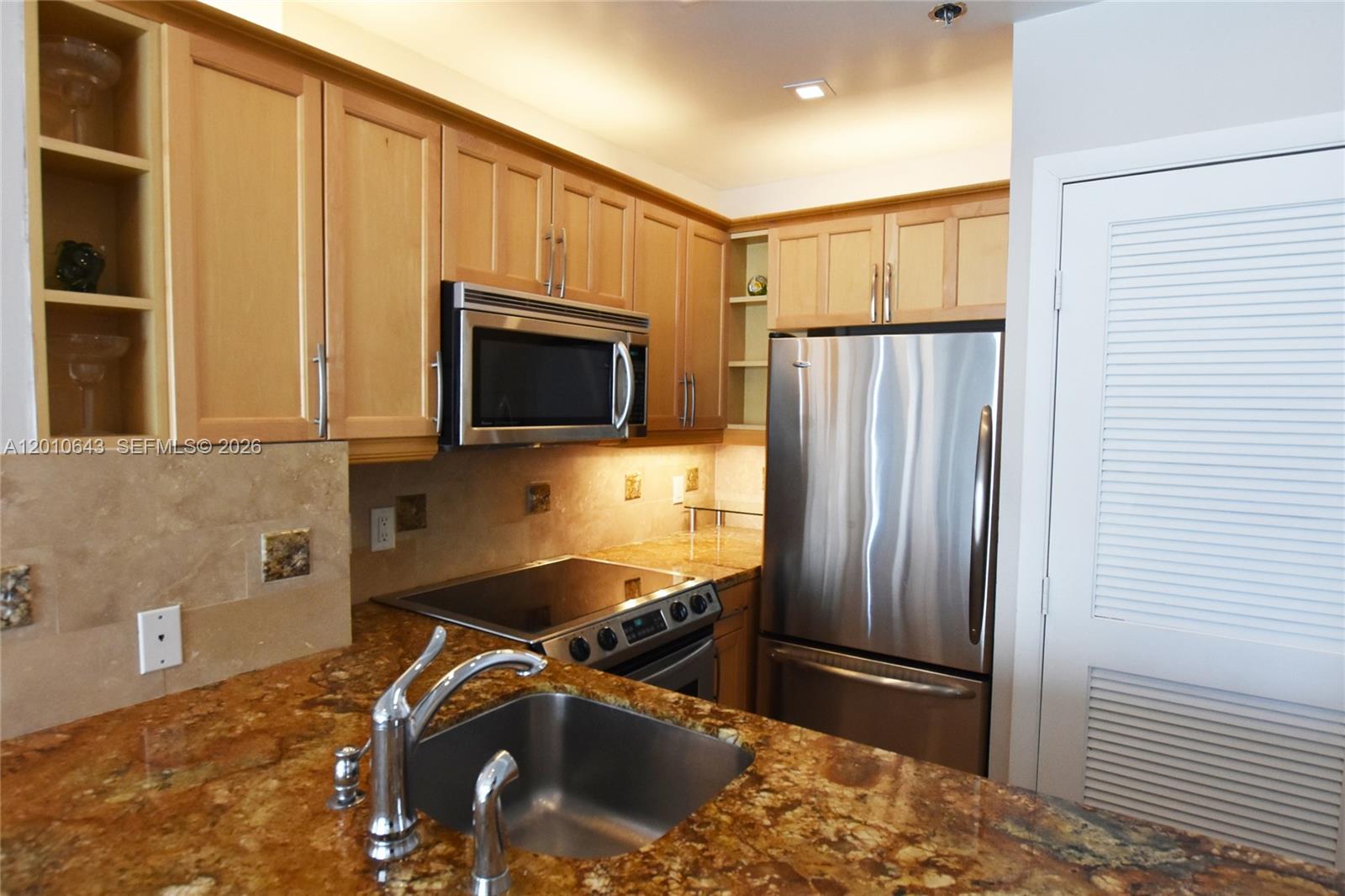A kitchen features light wood cabinets, granite countertops, stainless steel appliances, and a tiled backsplash — 540 Brickell Key Dr, Miami FL 33131, MIAMI, FL