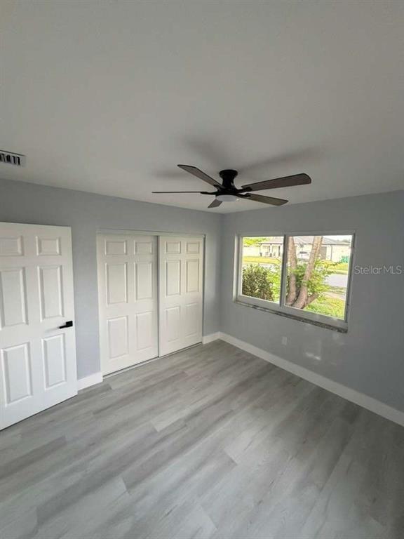 A bedroom with light gray walls, wood-look flooring, a ceiling fan, and white closet doors — 22202 BELINDA AVENUE, PORT CHARLOTTE, FL