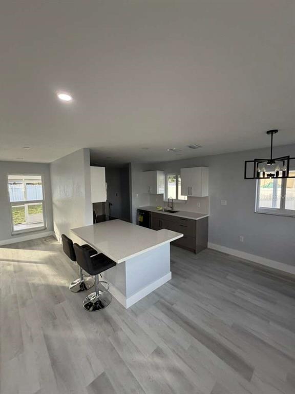A kitchen features a white island with bar stools, gray cabinetry, and light wood-look flooring — 22202 BELINDA AVENUE, PORT CHARLOTTE, FL