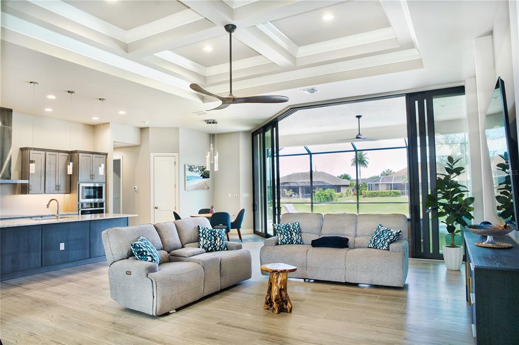 An open-concept living room and kitchen featuring a coffered ceiling and large sliding glass doors — 245 MARKER ROAD, ROTONDA WEST, FL