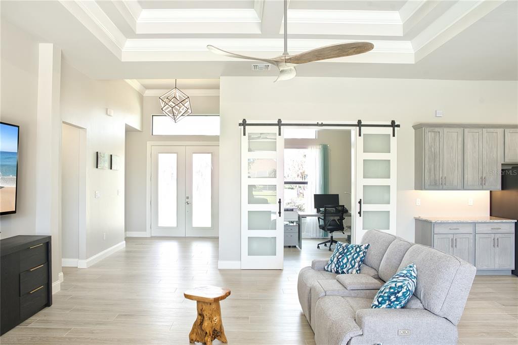 A living room features light wood-look tile floors, a tray ceiling, and sliding barn doors — 245 MARKER ROAD, ROTONDA WEST, FL
