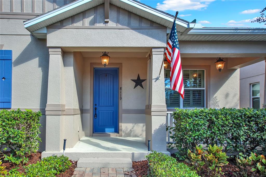 A front porch with a blue door, a hanging American flag, and a black star decoration — 8119 LAUGHING GULL STREET, WINTER GARDEN, FL