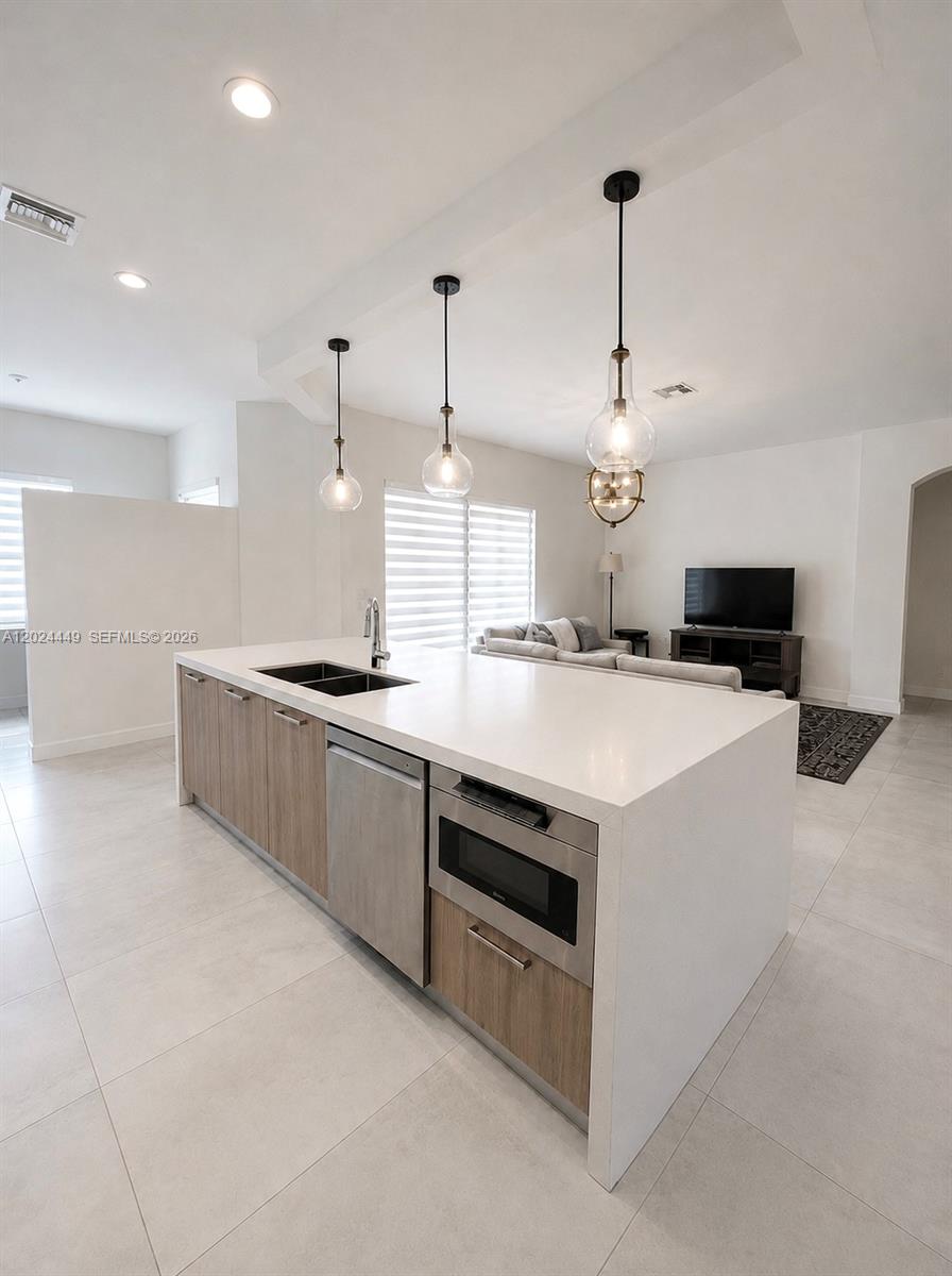 A modern kitchen island with a white countertop, wood cabinets, and stainless steel appliances — 4486 W Whitewater Ave, Weston FL 33332, WESTON, FL