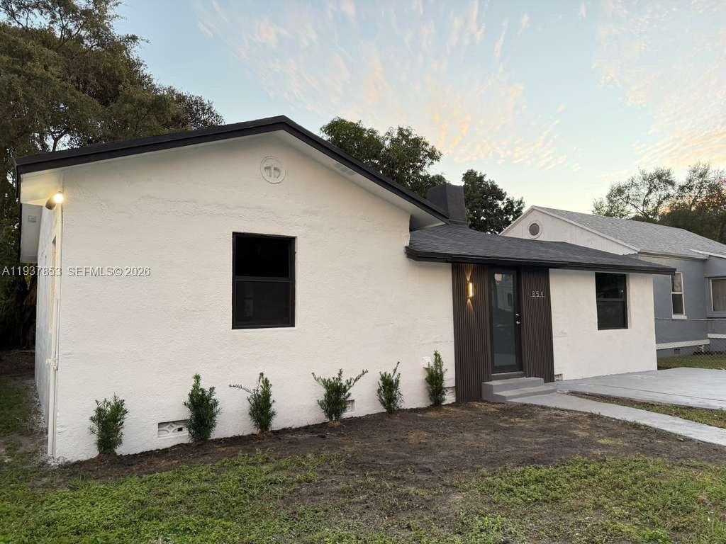 A white, single-story house features a dark-trimmed entryway, black window frames, and small shrubs — 854 NW 76th St, Miami FL 33150, MIAMI, FL
