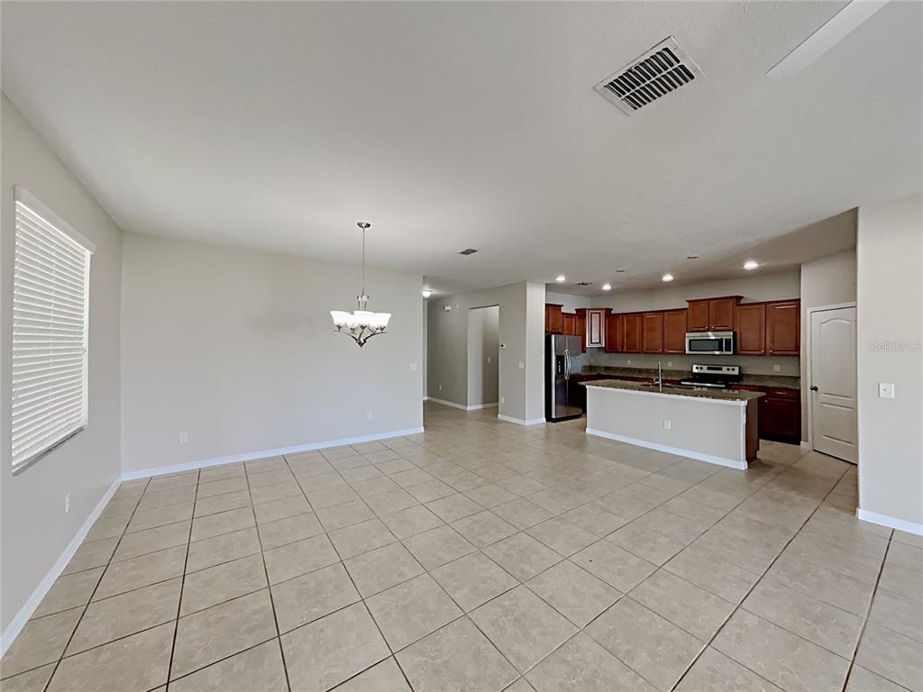 An open-concept living area features tile flooring, a dining space with a chandelier, and a kitchen — 1821 PENRITH LOOP, ORLANDO, FL