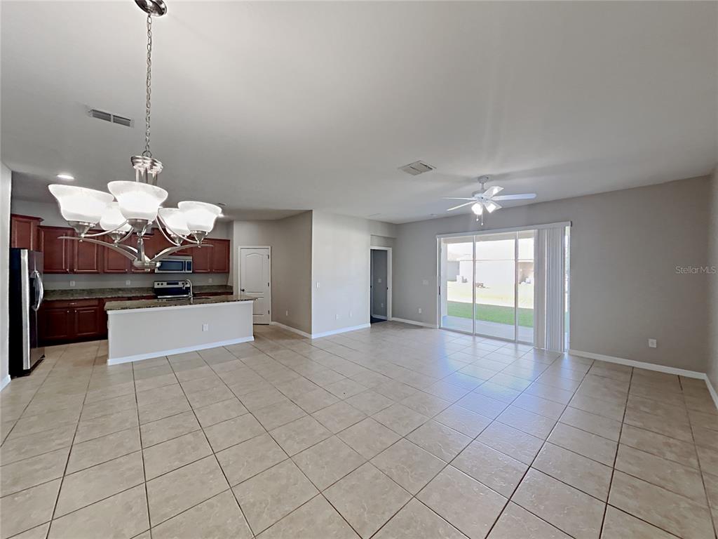 An open-concept kitchen and living area features tile flooring, dark wood cabinets, and sliding doors — 1821 PENRITH LOOP, ORLANDO, FL