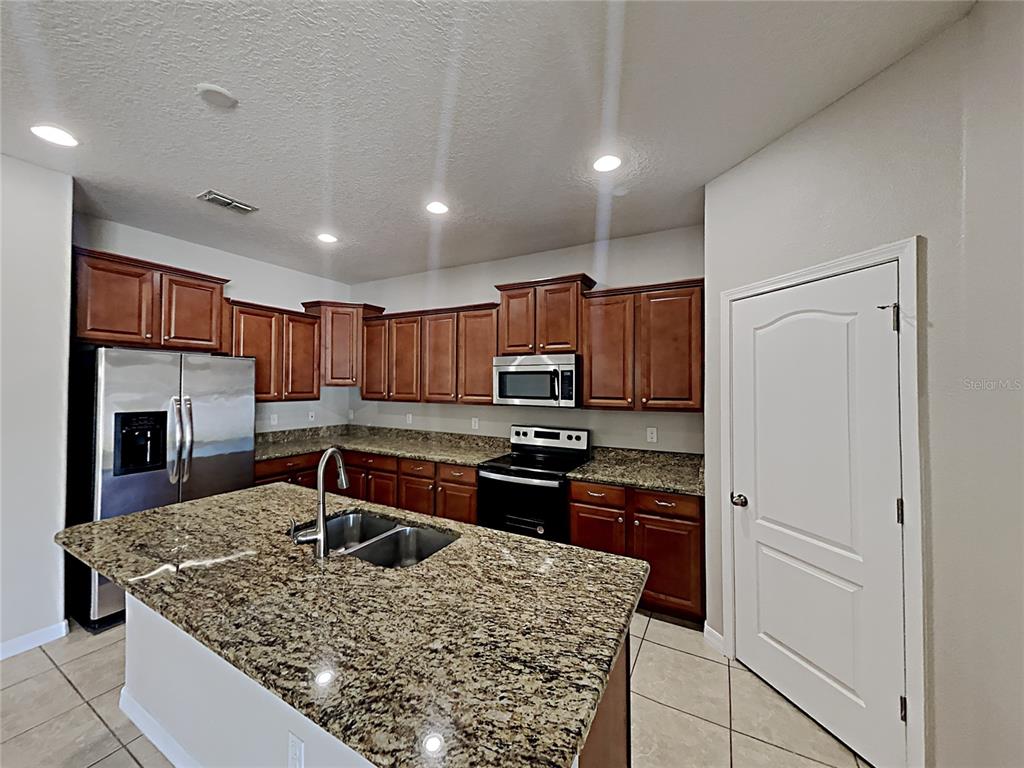 A kitchen features wood cabinets, granite countertops, a center island, and stainless steel appliances — 1821 PENRITH LOOP, ORLANDO, FL