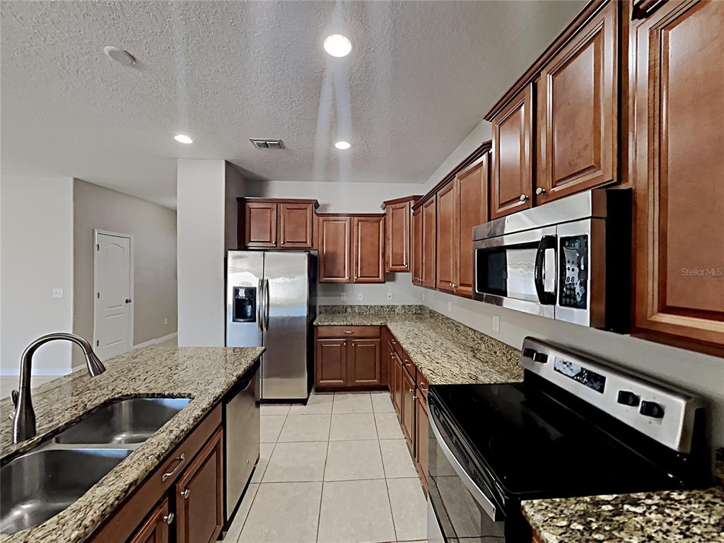 A kitchen features wood cabinets, granite countertops, stainless steel appliances, and tile flooring — 1821 PENRITH LOOP, ORLANDO, FL
