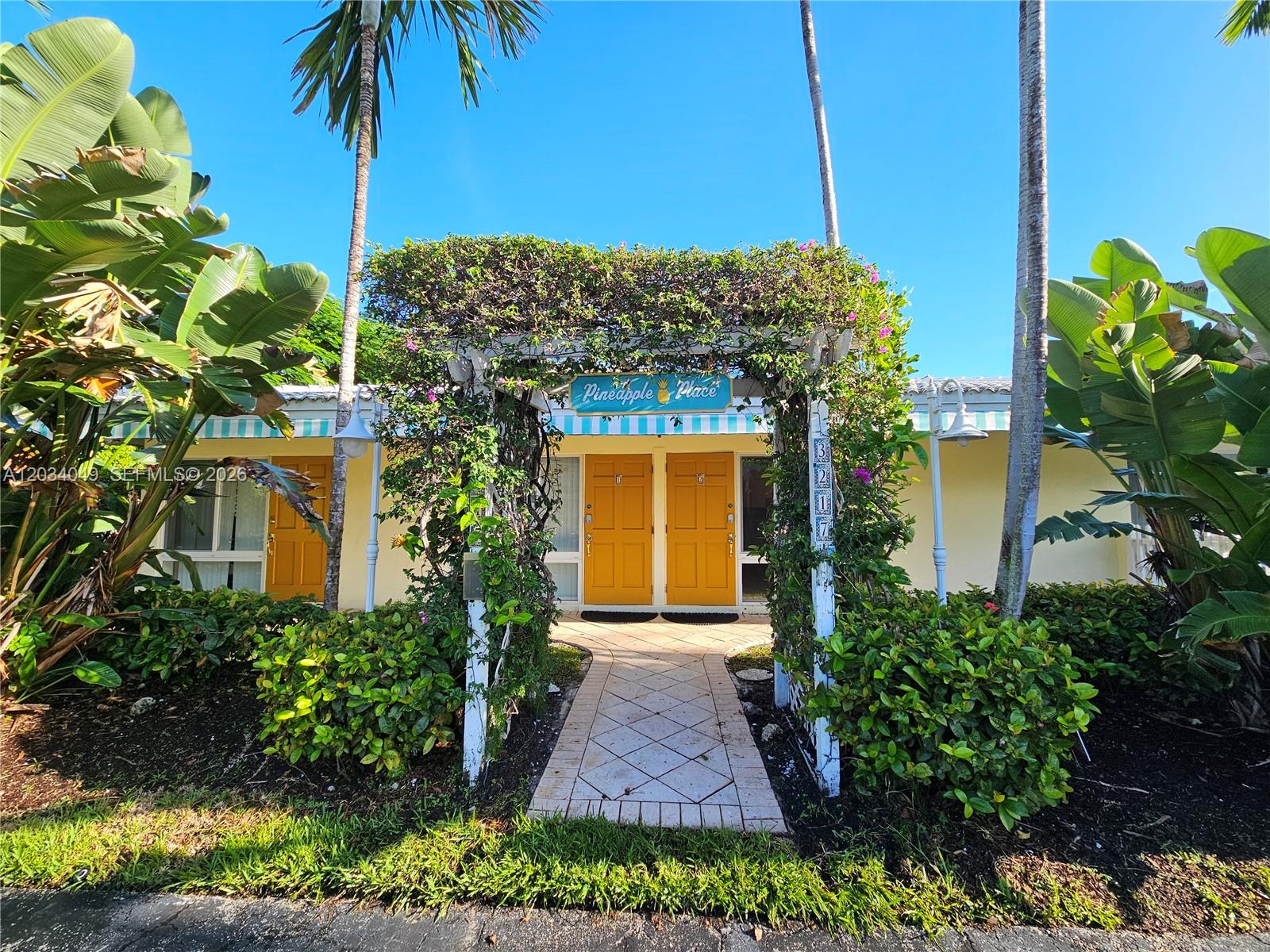A walkway leads through a vine-covered trellis to two yellow doors at a building entrance — 3217 NE 7th Pl # 4, Pompano Beach FL 33062, POMPANO BEACH, FL