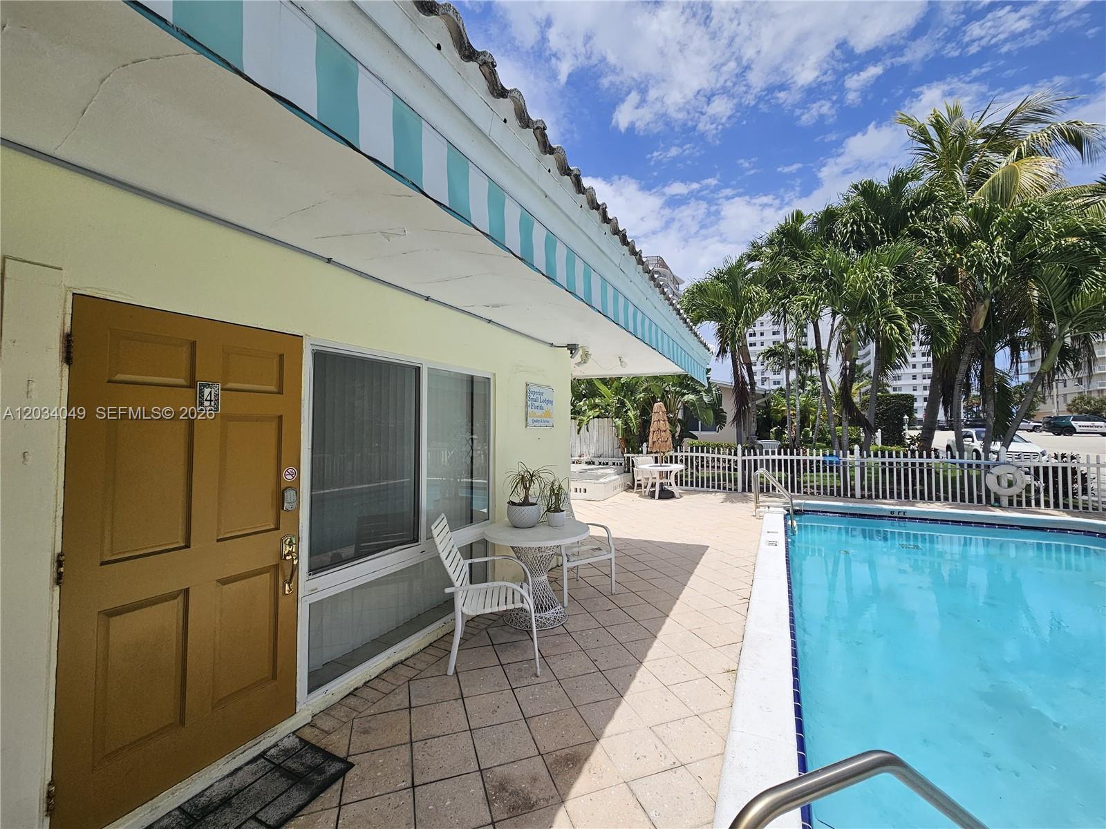 A tan building with a striped awning sits beside a swimming pool on a patio — 3217 NE 7th Pl # 4, Pompano Beach FL 33062, POMPANO BEACH, FL
