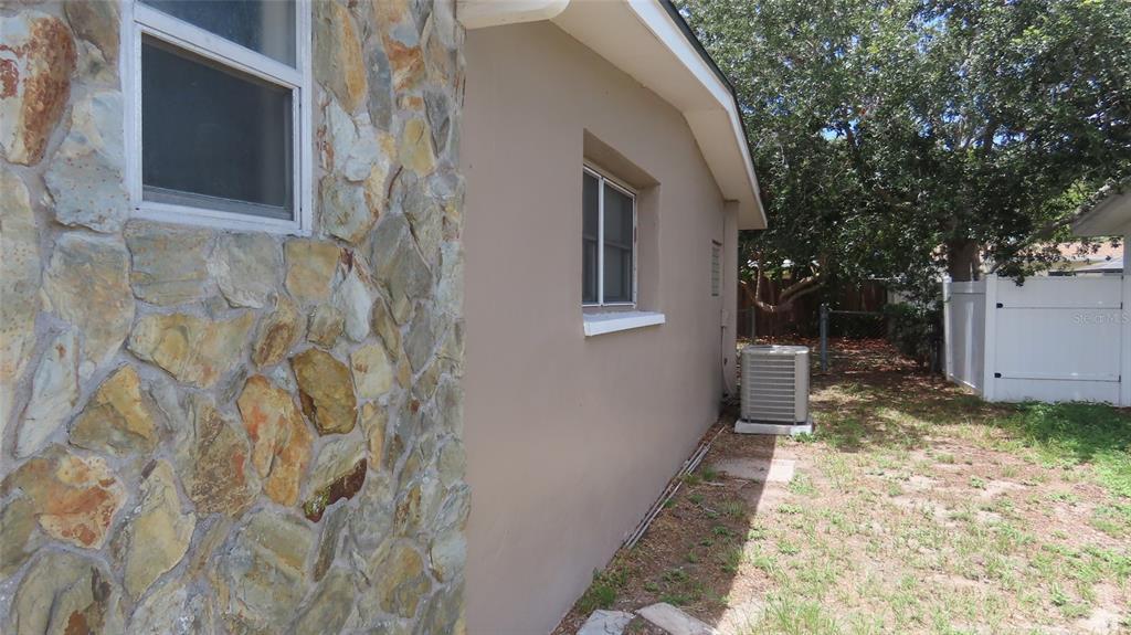 The exterior side of a house features a stone facade, stucco walls, and an air conditioner — 12208 105TH STREET, LARGO, FL