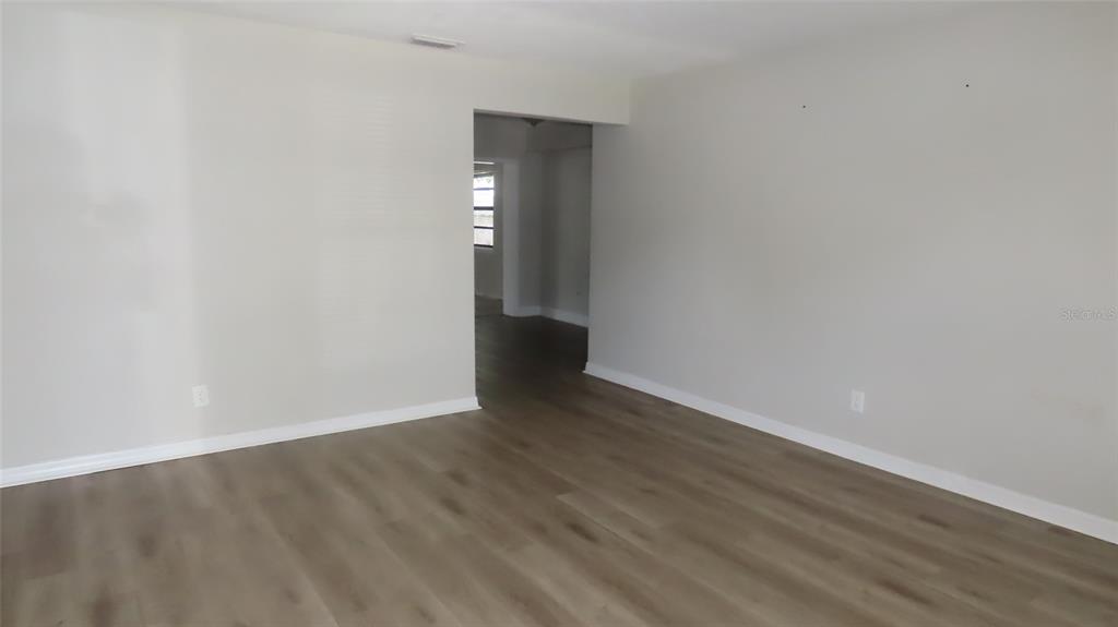 An empty room with light gray walls and wood-look flooring leads to an adjacent space — 12208 105TH STREET, LARGO, FL