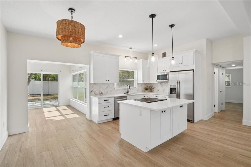 A white kitchen features a center island, stainless steel appliances, and light wood-look flooring — 6765 W FLAMINGO WAY S, ST PETERSBURG, FL
