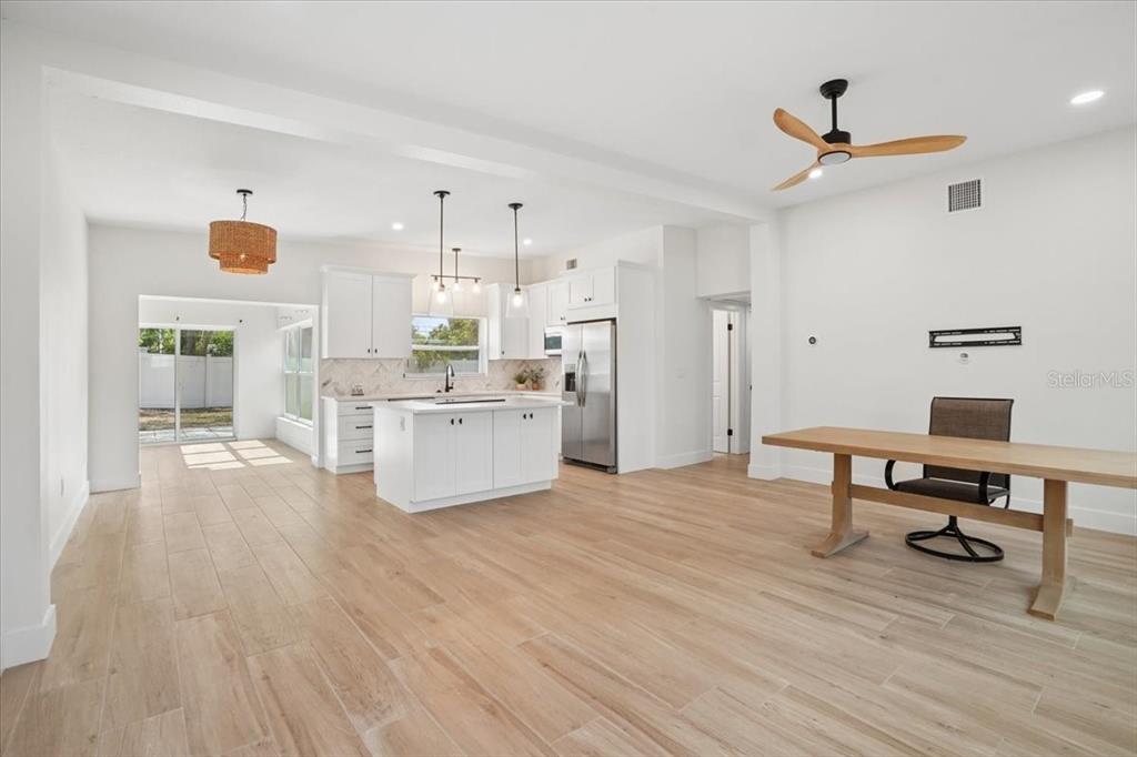 A bright, open-concept kitchen and dining area features white cabinetry, a central island, and wood-look flooring — 6765 W FLAMINGO WAY S, ST PETERSBURG, FL