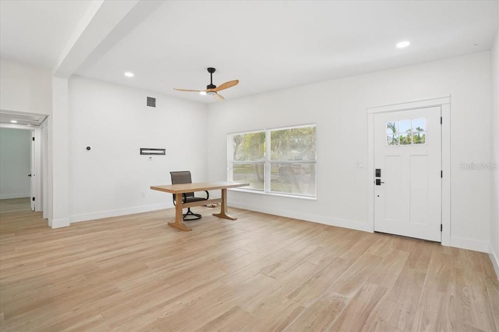 A bright, minimalist room features light wood-look flooring, white walls, a ceiling fan, and a desk — 6765 W FLAMINGO WAY S, ST PETERSBURG, FL