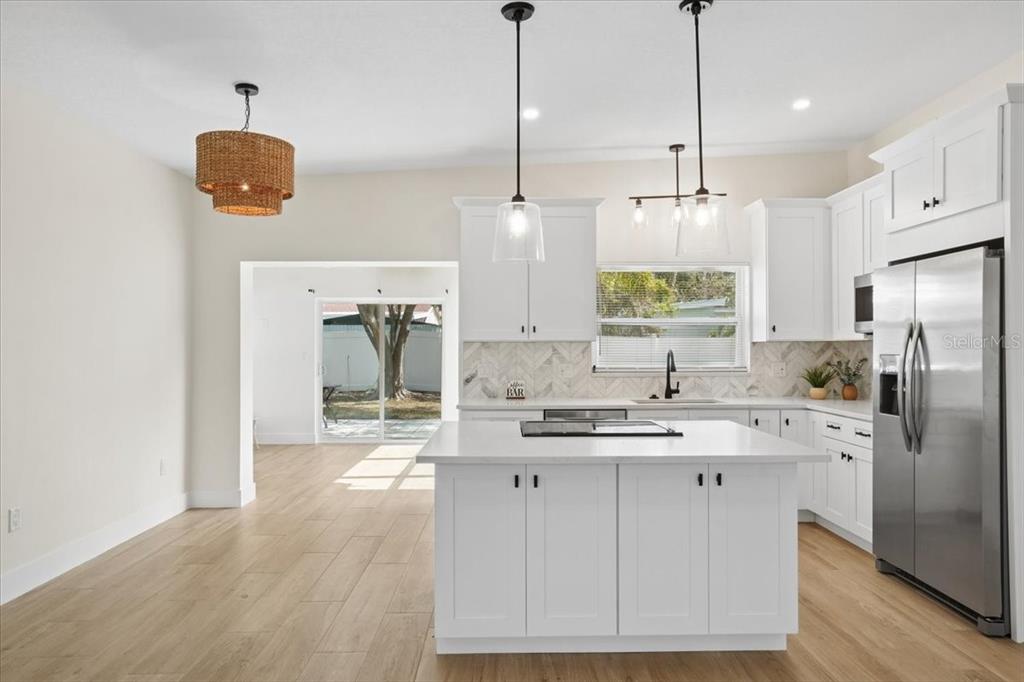 A bright kitchen features white cabinets, a central island, and wood-look flooring — 6765 W FLAMINGO WAY S, ST PETERSBURG, FL