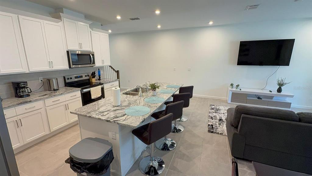 A modern open-concept kitchen features white cabinetry, granite countertops, and an island with bar seating — 2334 ZABALLINA PLACE UNIT 2343, KISSIMMEE, FL